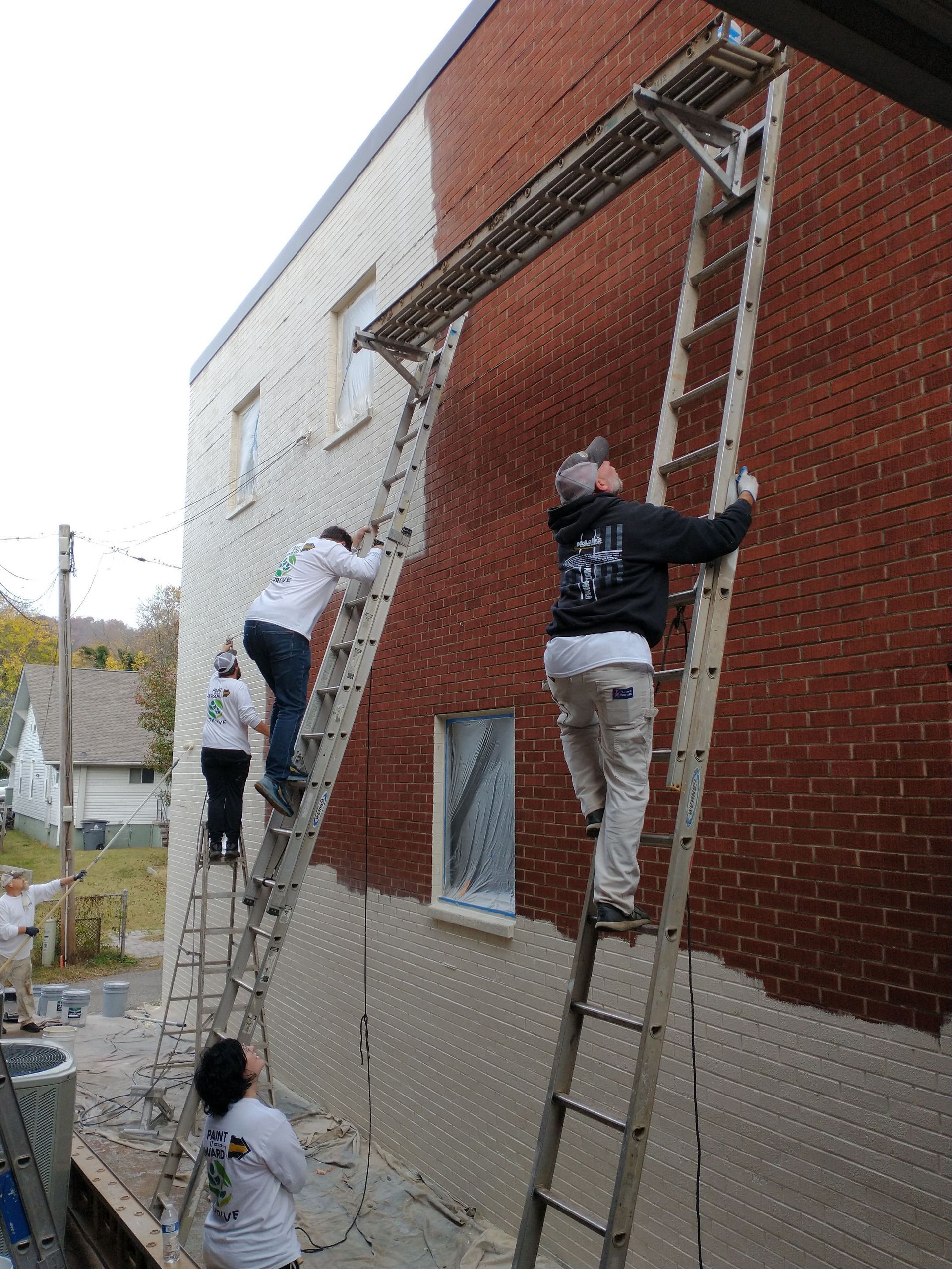 A group of people are painting a brick building with ladders.