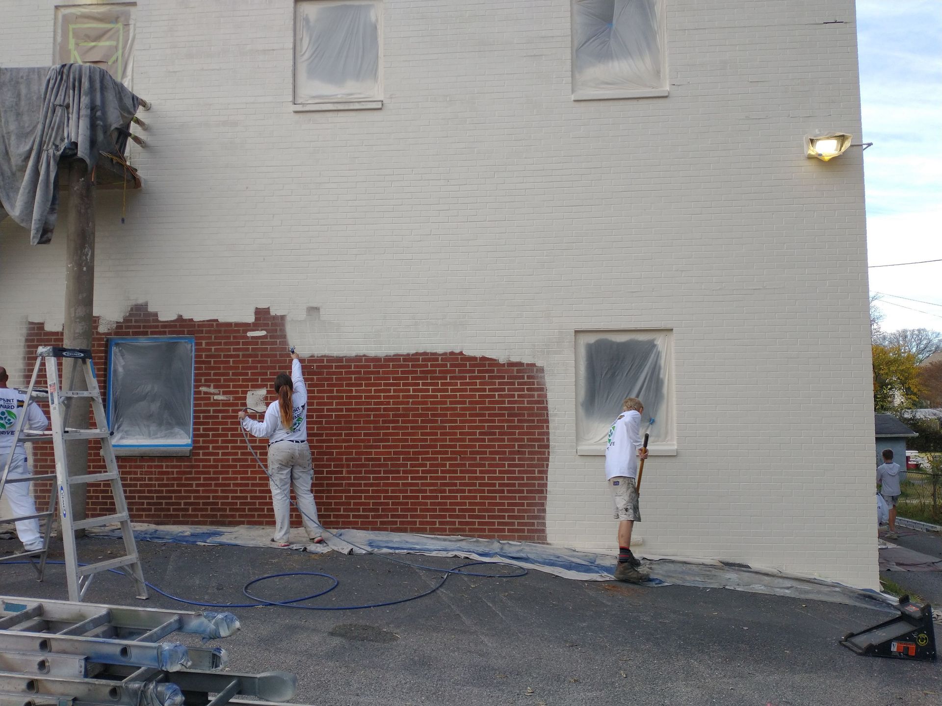 Two people are painting a brick building white