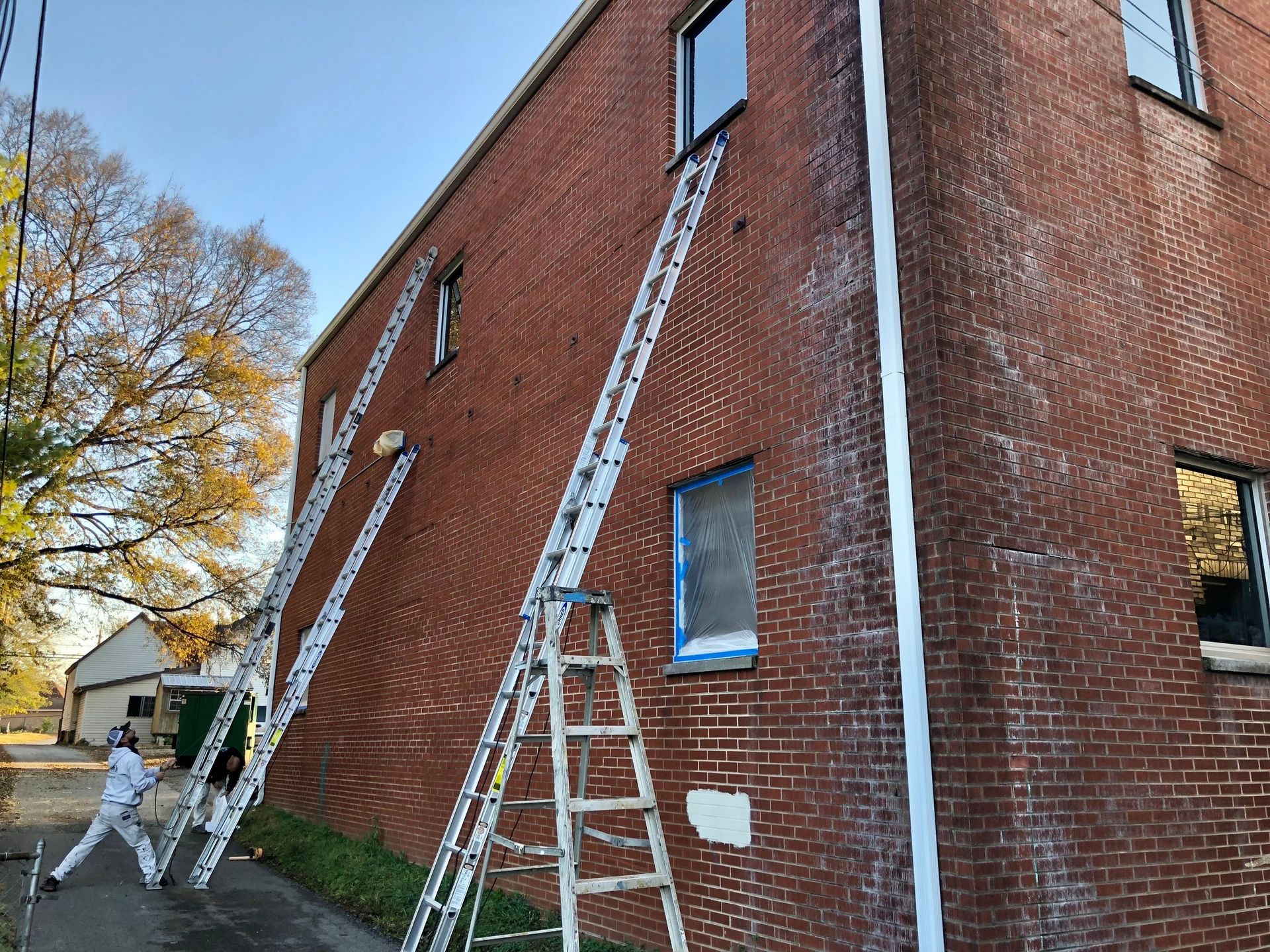 A man is painting the side of a brick building with ladders.