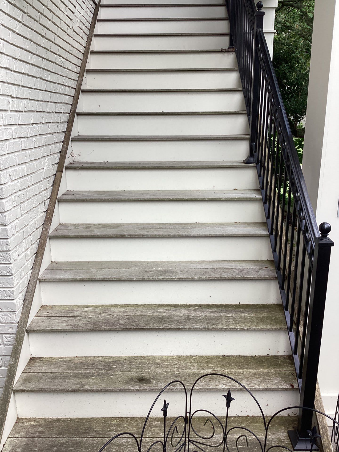 A set of stairs leading up to a porch with a black railing.