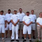 A group of men in white shirts and shorts are standing in front of a brick wall.