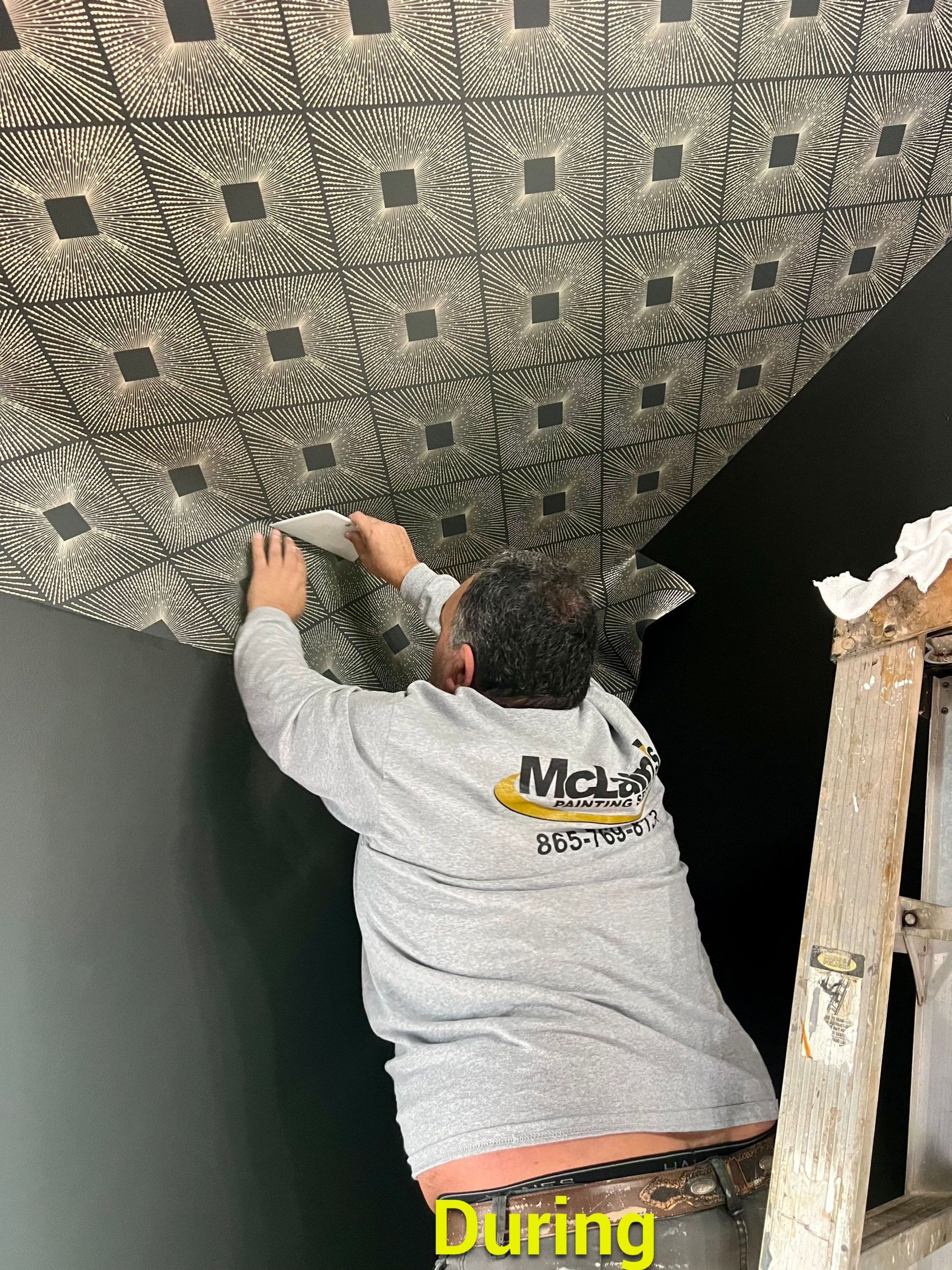 A man is standing on a ladder applying wallpaper to a ceiling.