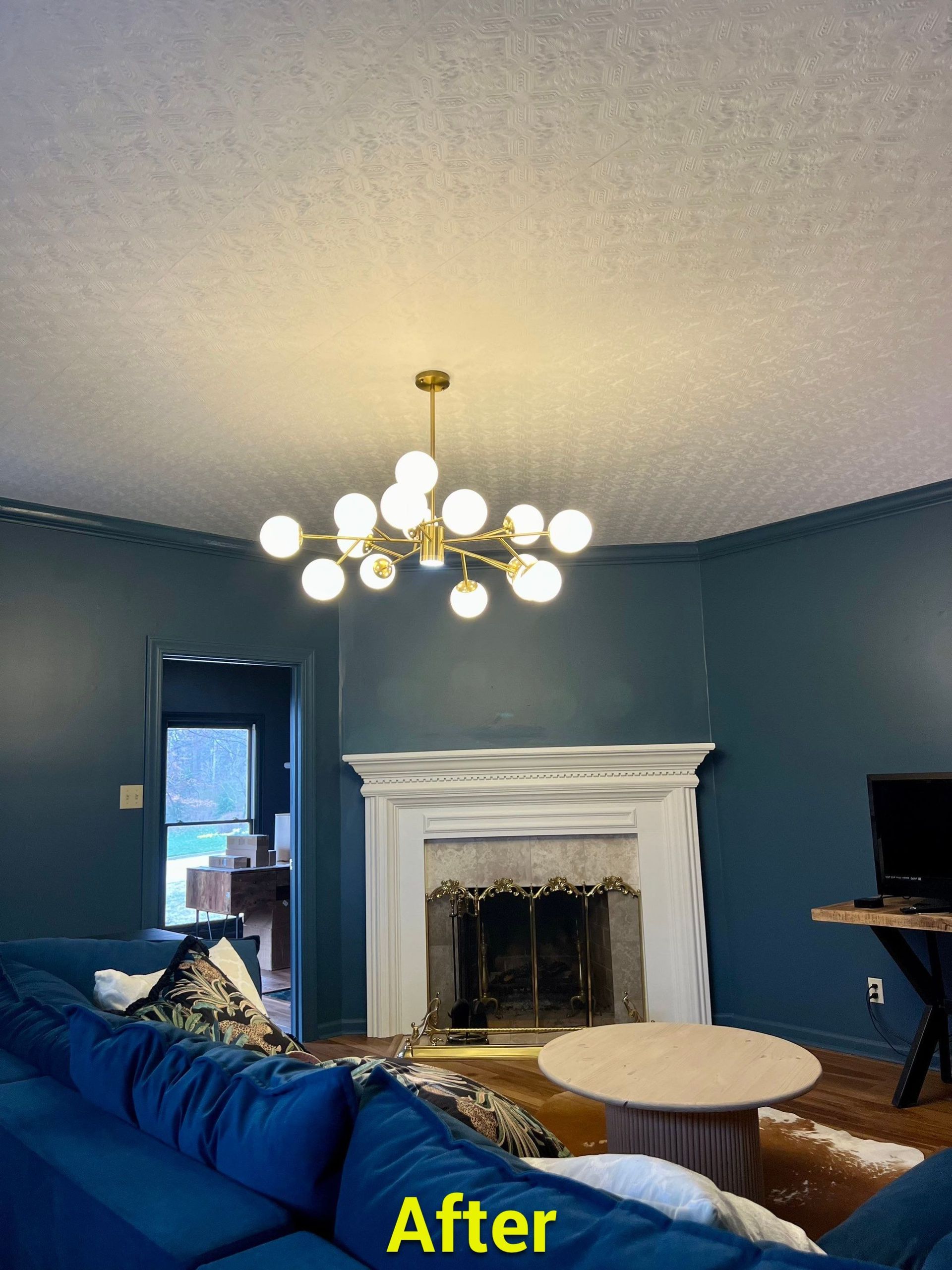 A living room with blue walls and a fireplace and a chandelier hanging from the ceiling.