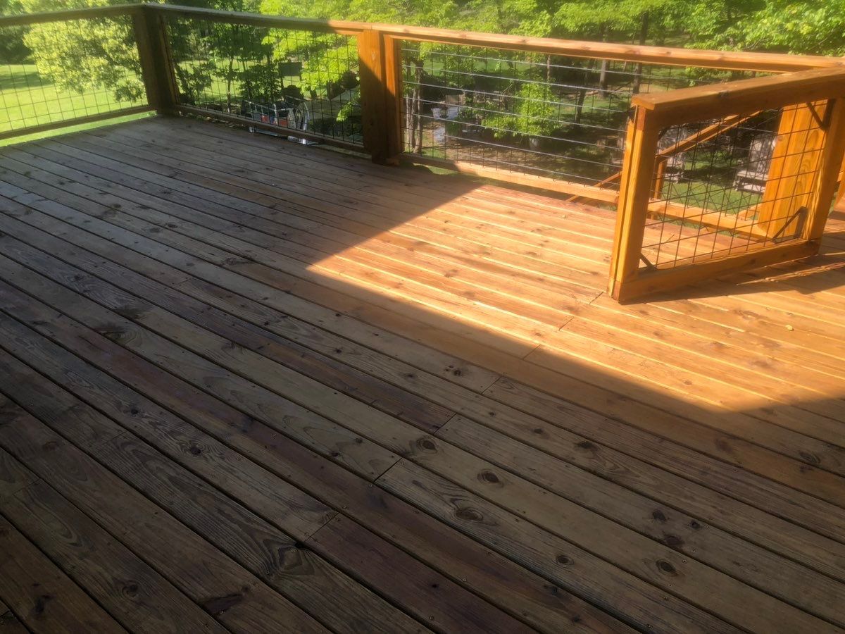 A wooden deck with a fence and trees in the background.