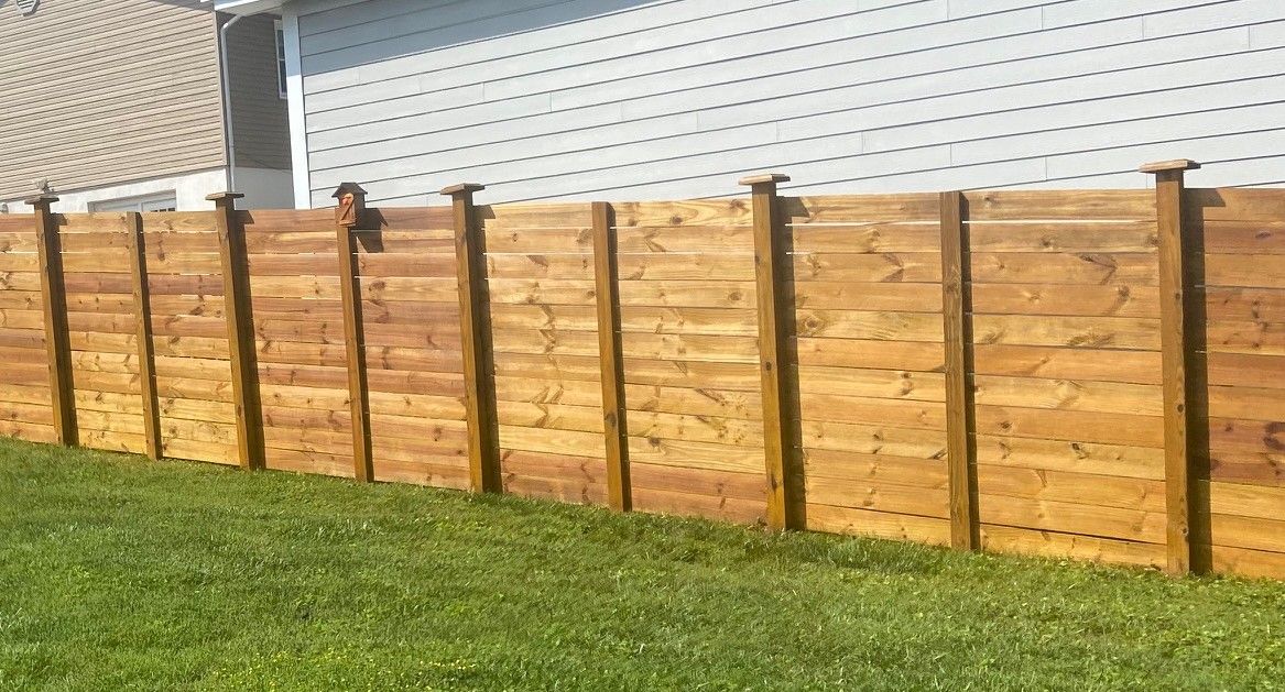 A wooden fence is sitting in the grass in front of a house.