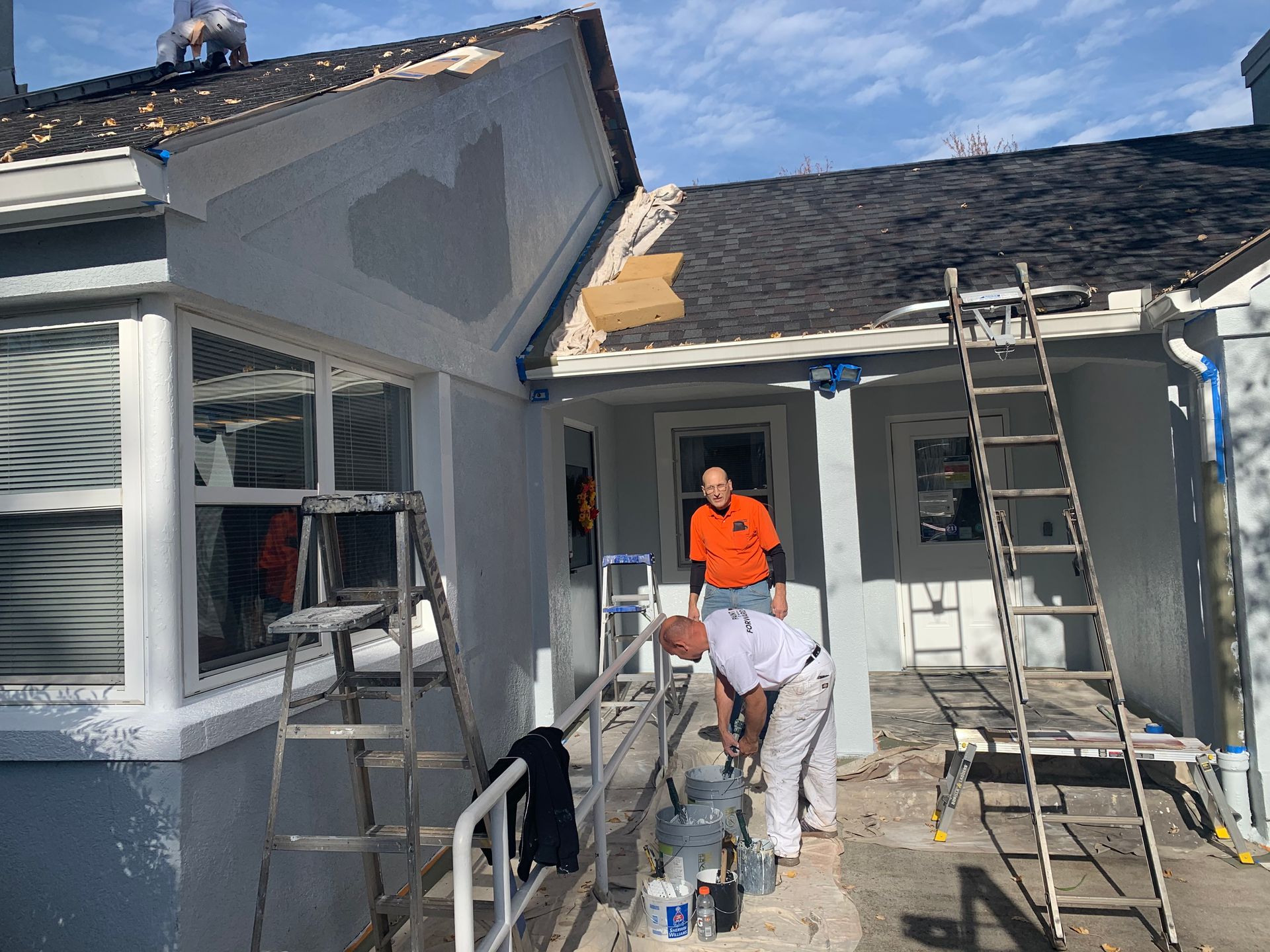 A man is painting the side of a house with a ladder.