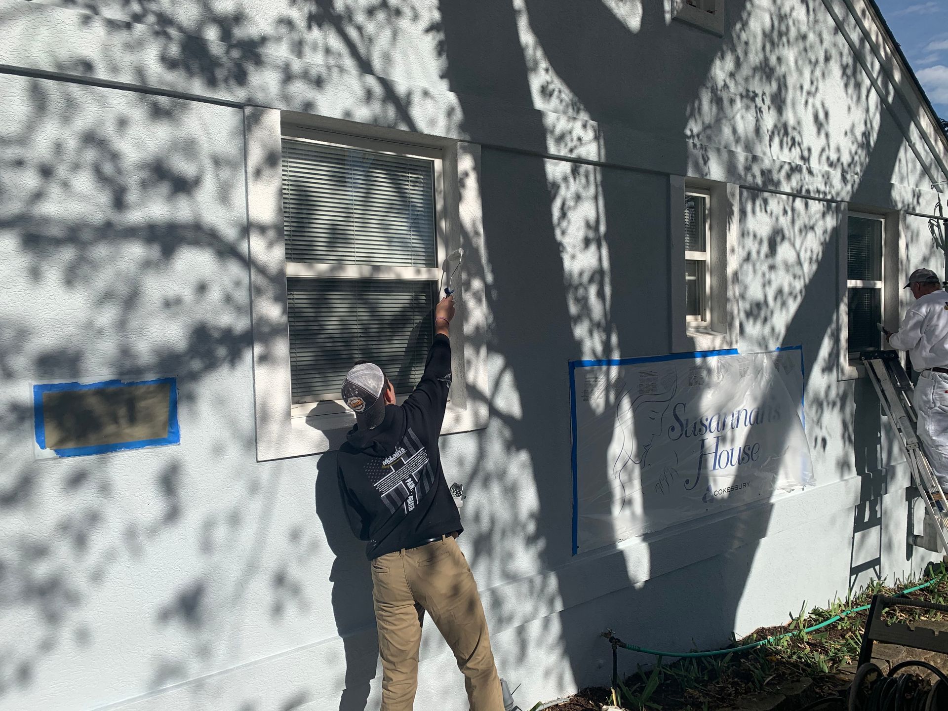A man is painting a window on the side of a house.