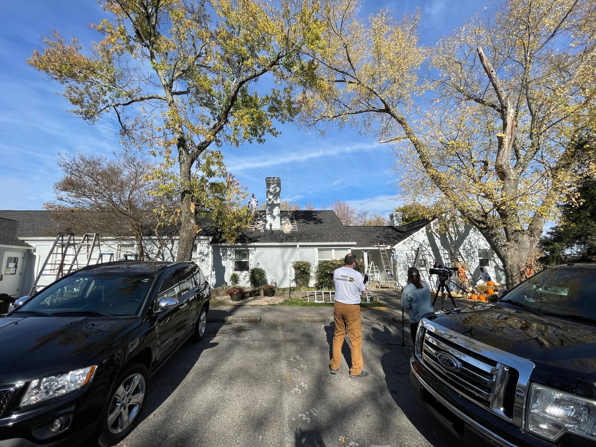 A man is standing in front of a house with cars parked in front of it.