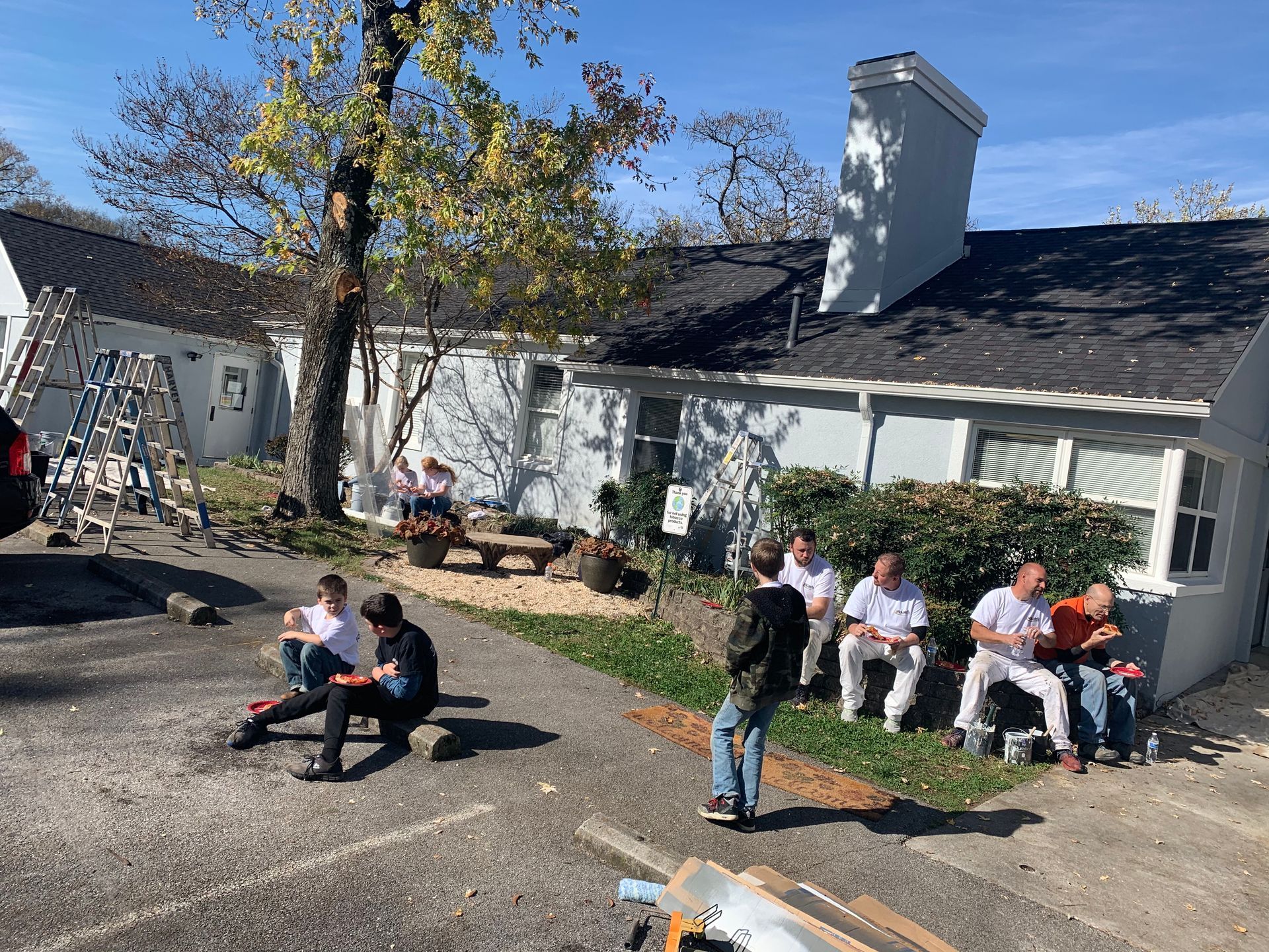 A group of people are sitting on the sidewalk in front of a house.
