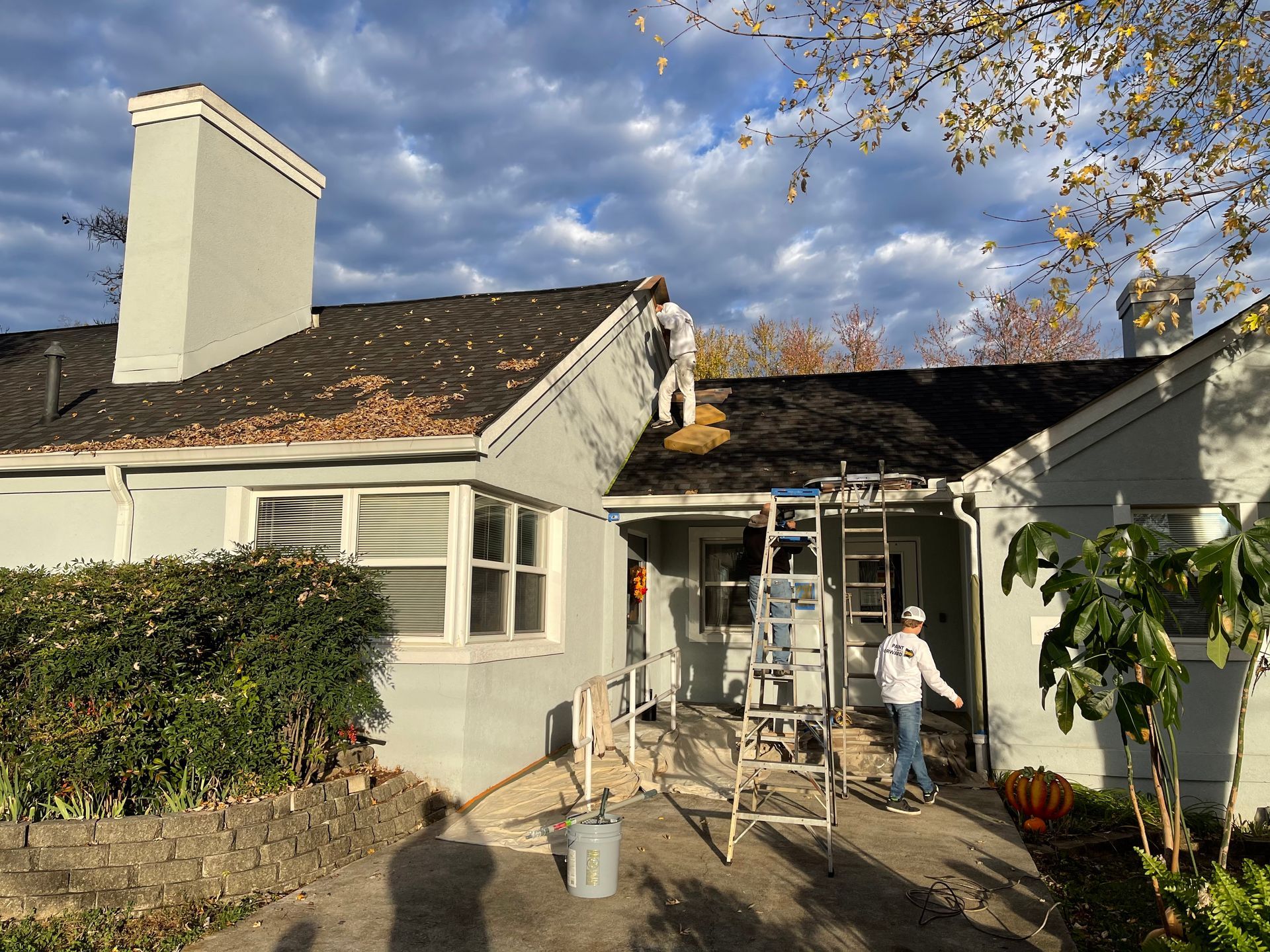 A man is standing on a ladder on the roof of a house.