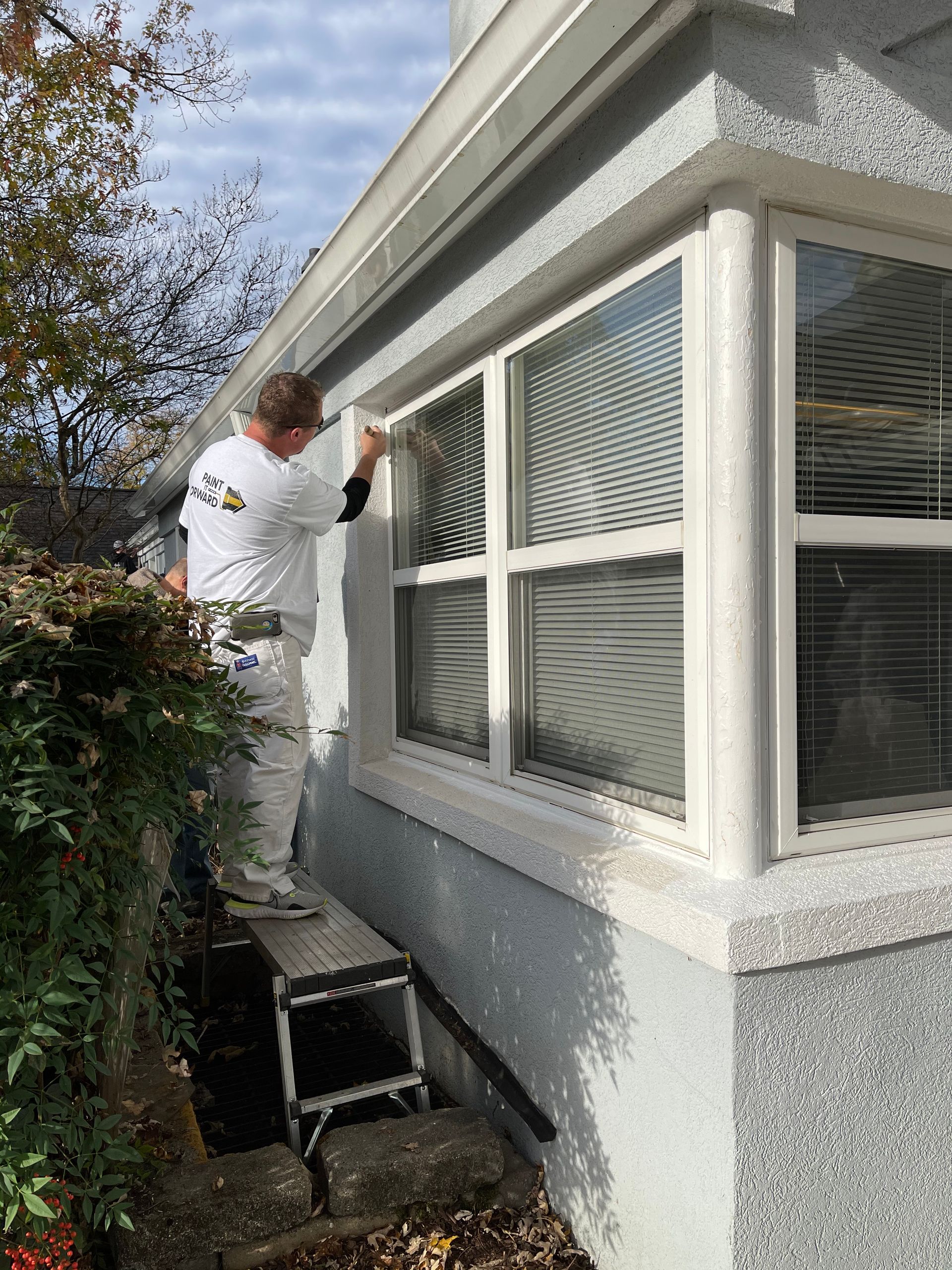 A man is painting a window on the side of a house.