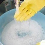 A person wearing yellow rubber gloves is cleaning a sink with a plunger.