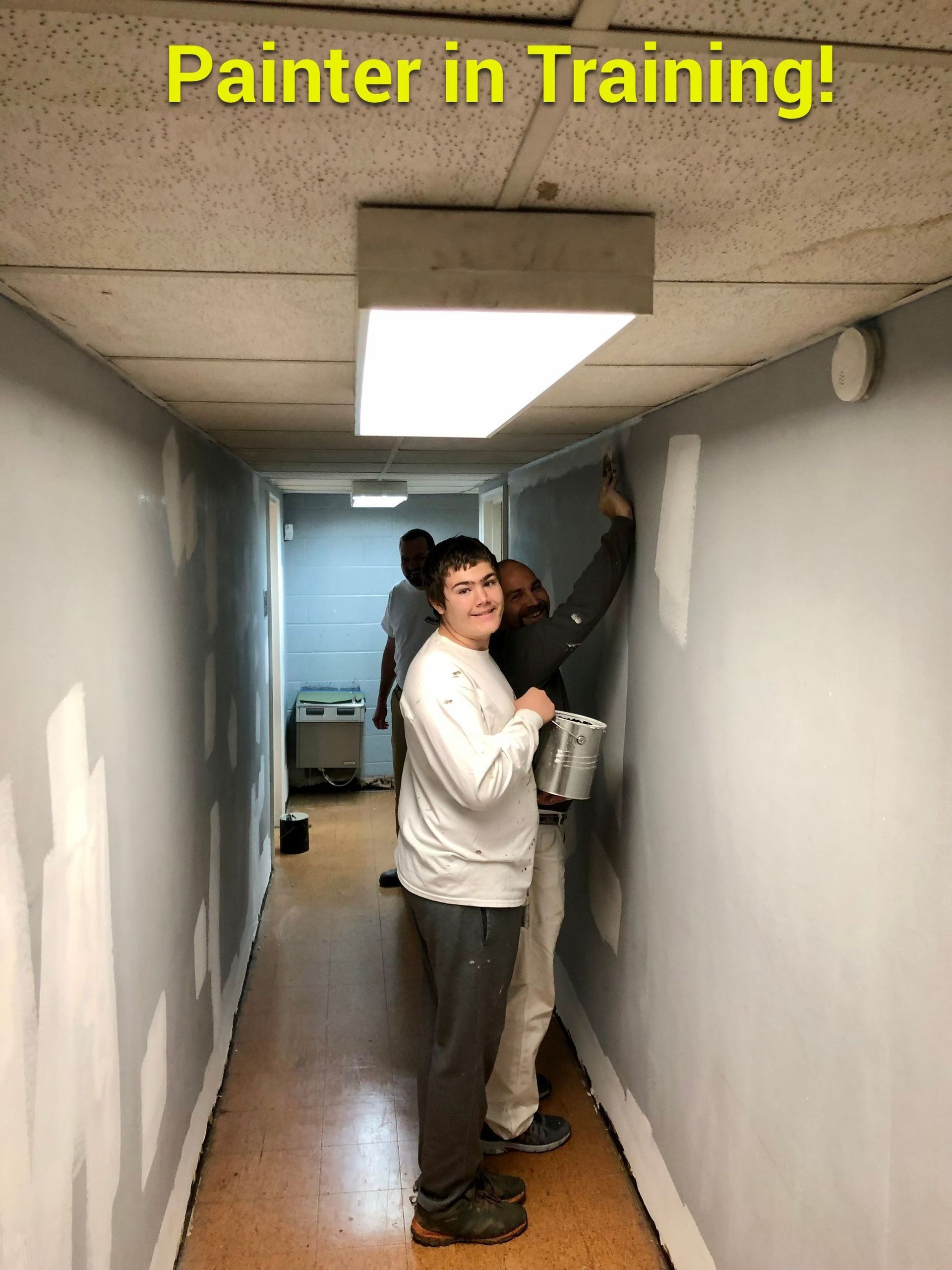A group of people are painting a wall in a hallway.