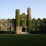 A large brick building with a tower on top of it is surrounded by ivy.