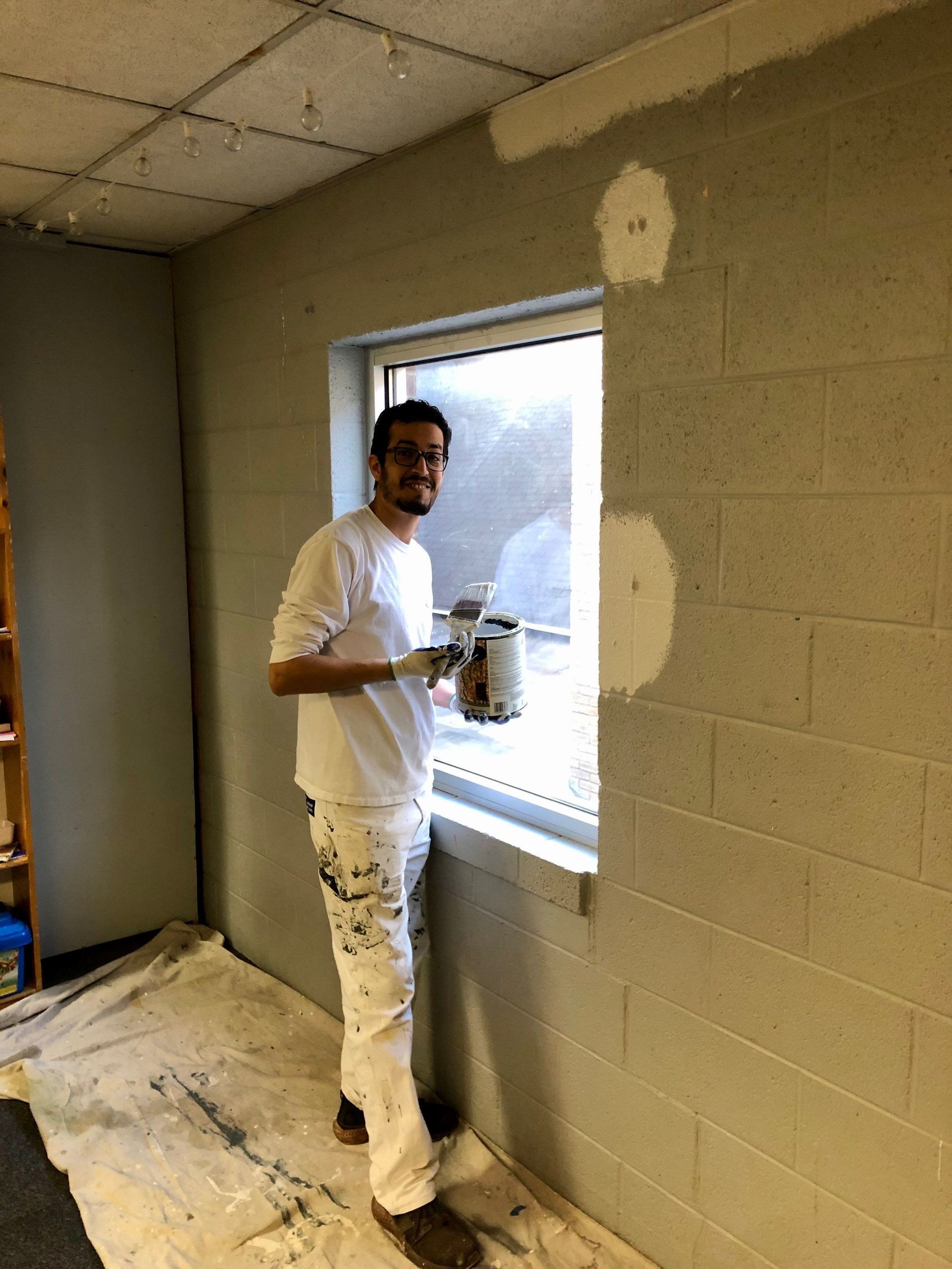 A man is painting a wall next to a window.