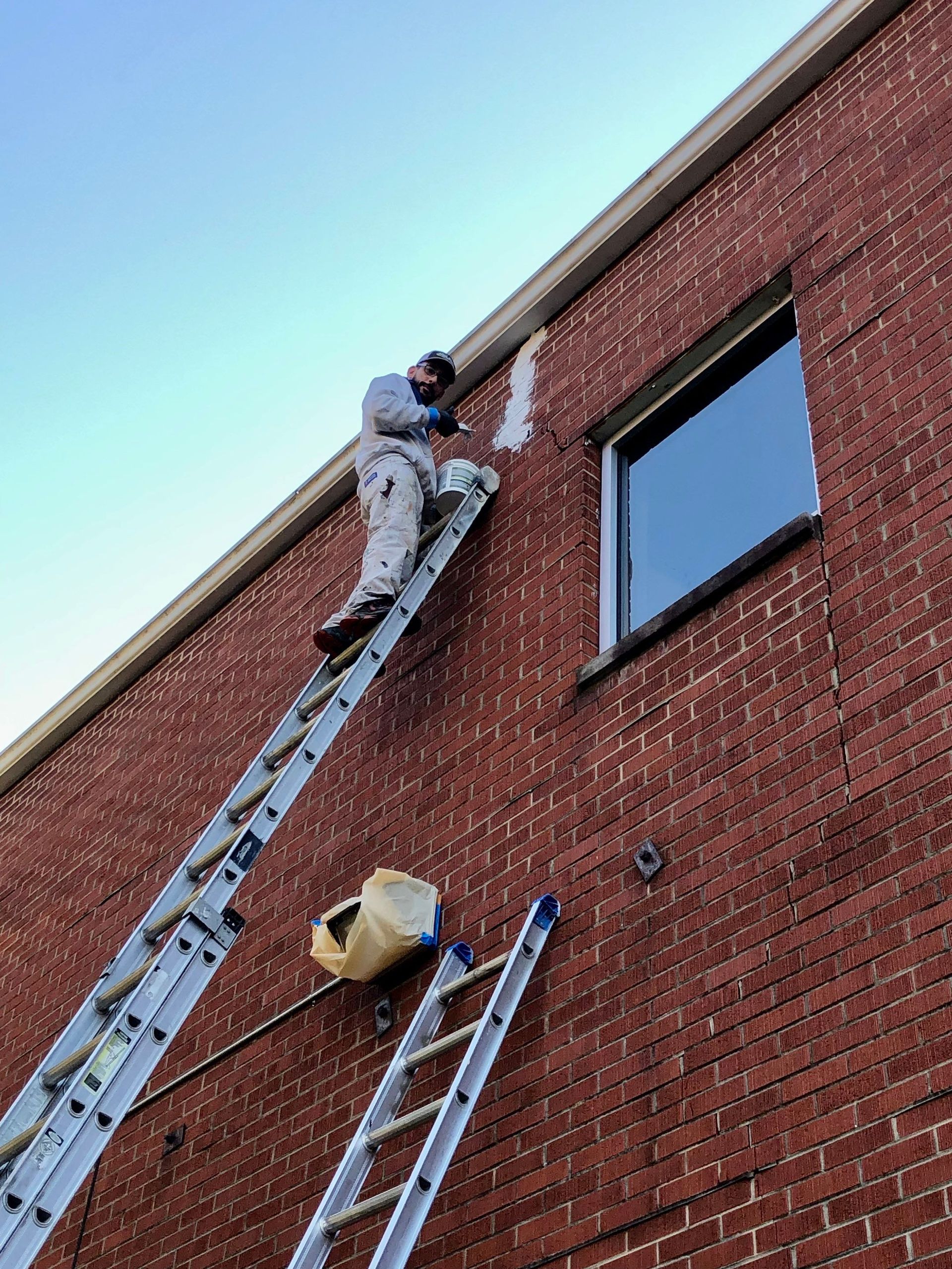 A man is standing on a ladder on the side of a brick building