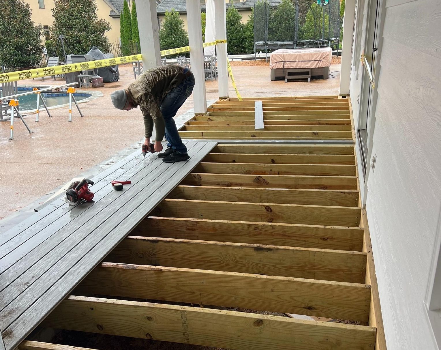 A man is working on a wooden deck under a porch.