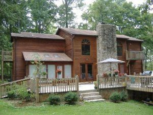 A large wooden house with a stone chimney and a large deck surrounded by trees.