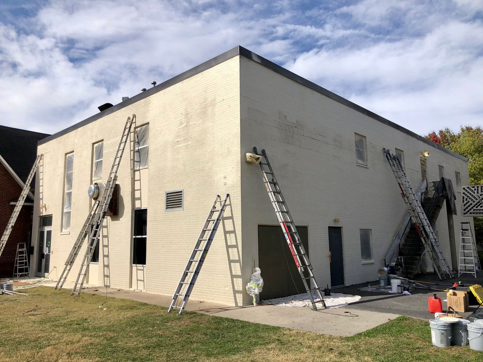 A large white building is being painted with ladders.