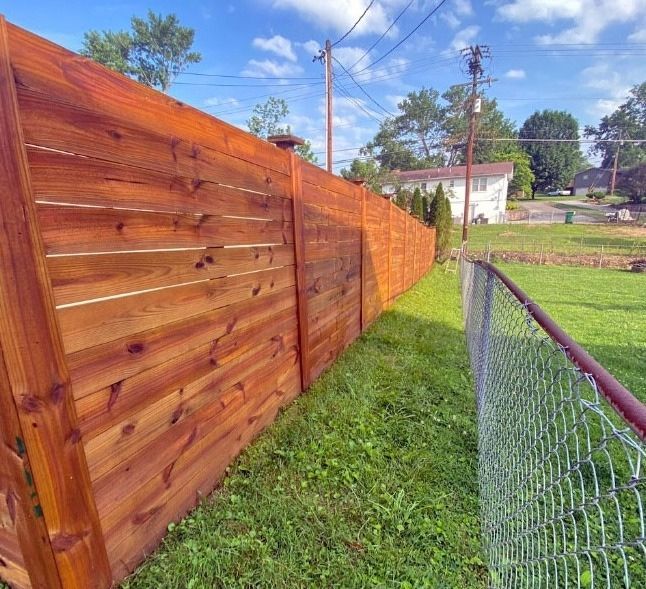 A wooden fence is surrounded by grass and a chain link fence.