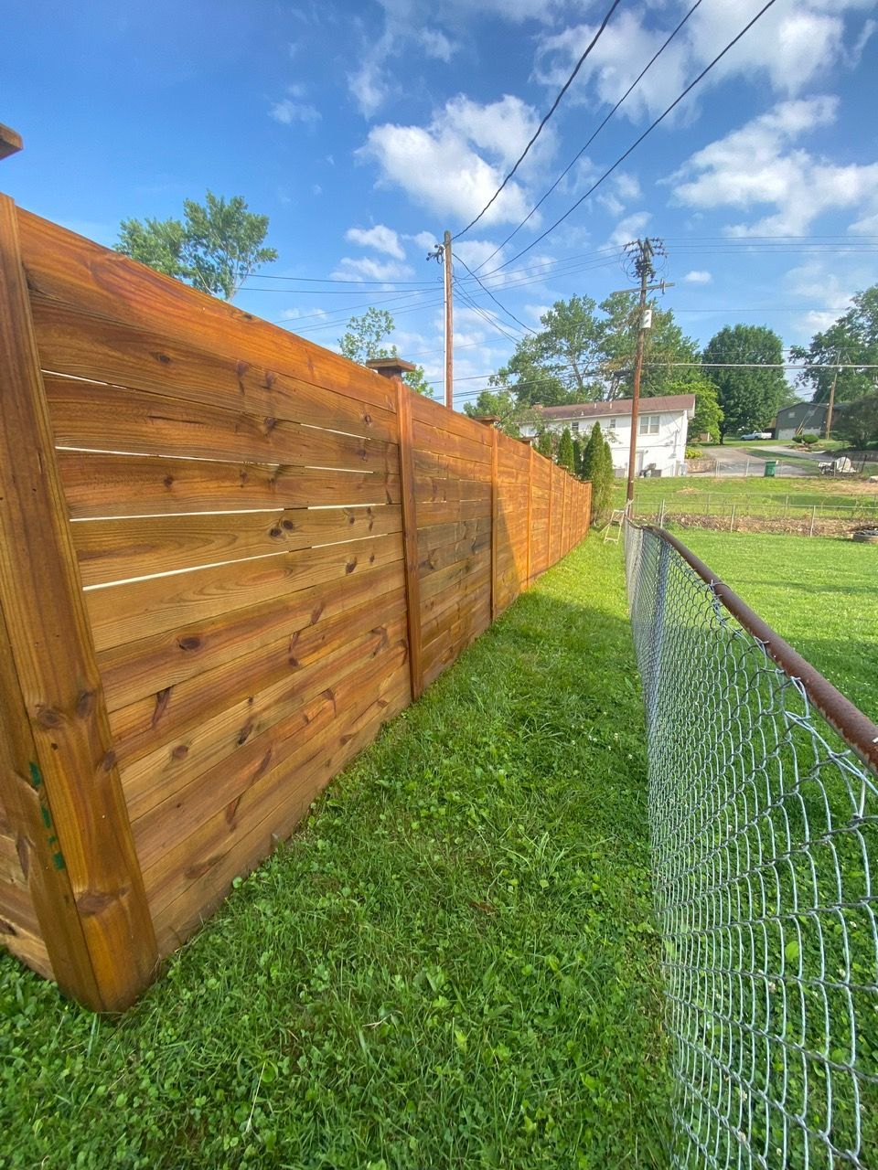 A wooden fence surrounds a lush green yard next to a chain link fence.