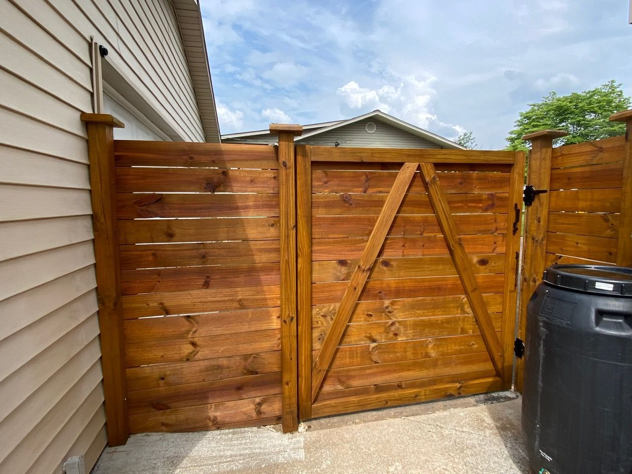 A wooden gate is sitting in front of a house next to a trash can.