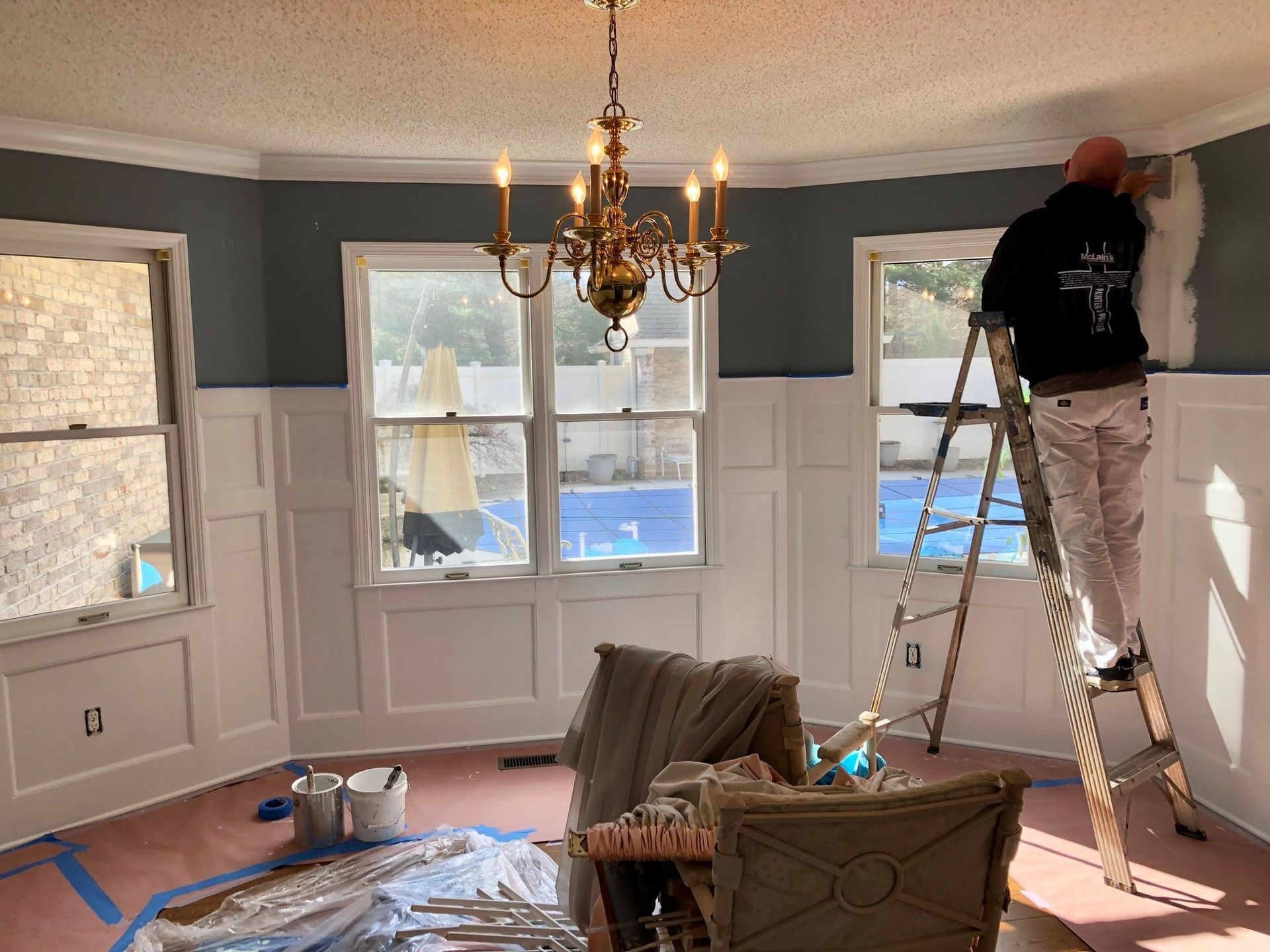 A man is standing on a ladder in a living room painting the walls.