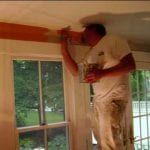 A man is painting the ceiling of a room in front of a window.