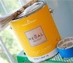 A can of yellow paint with a brush in it is sitting on a table next to a window.