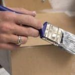 A person is painting a piece of wood with a paint brush.