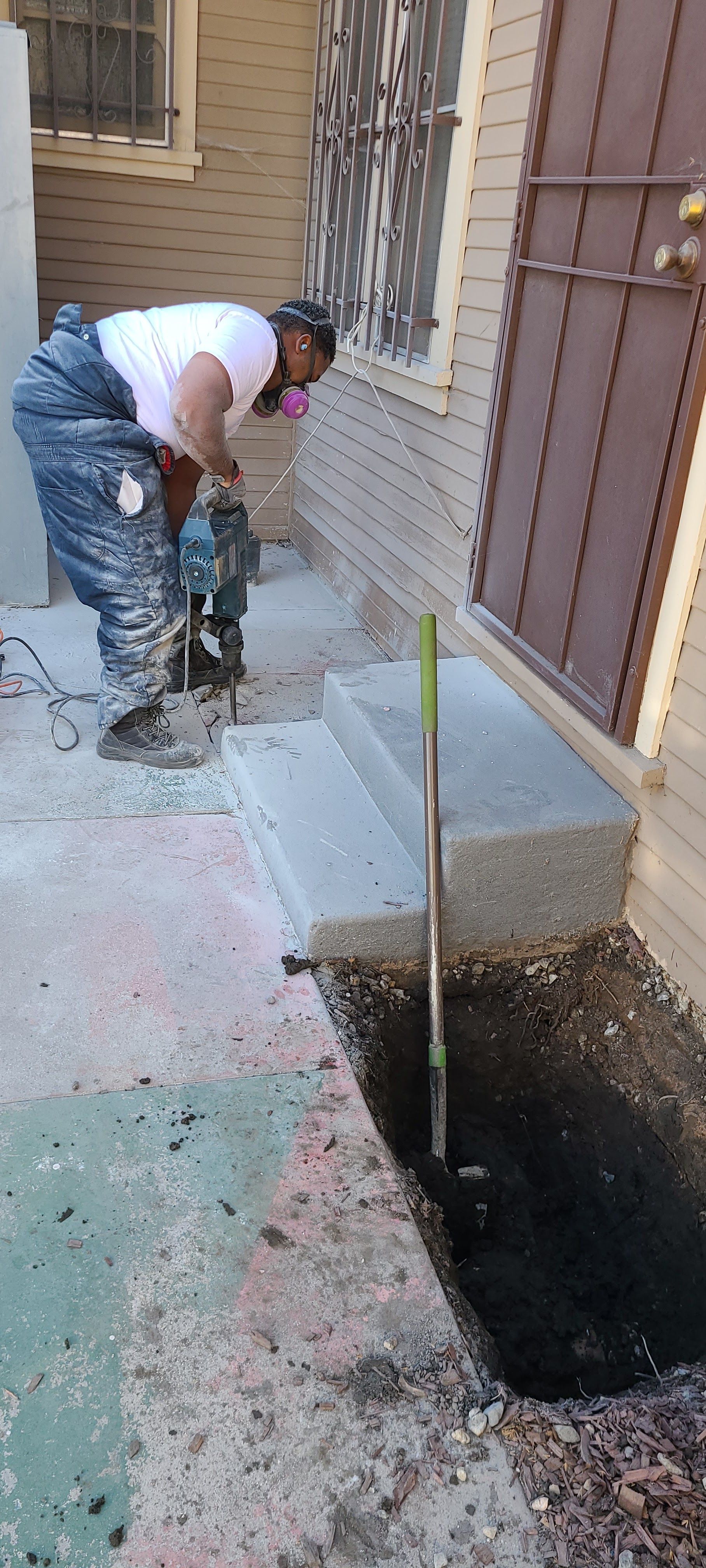 A man is using a drill to dig a hole in the ground in front of a house.