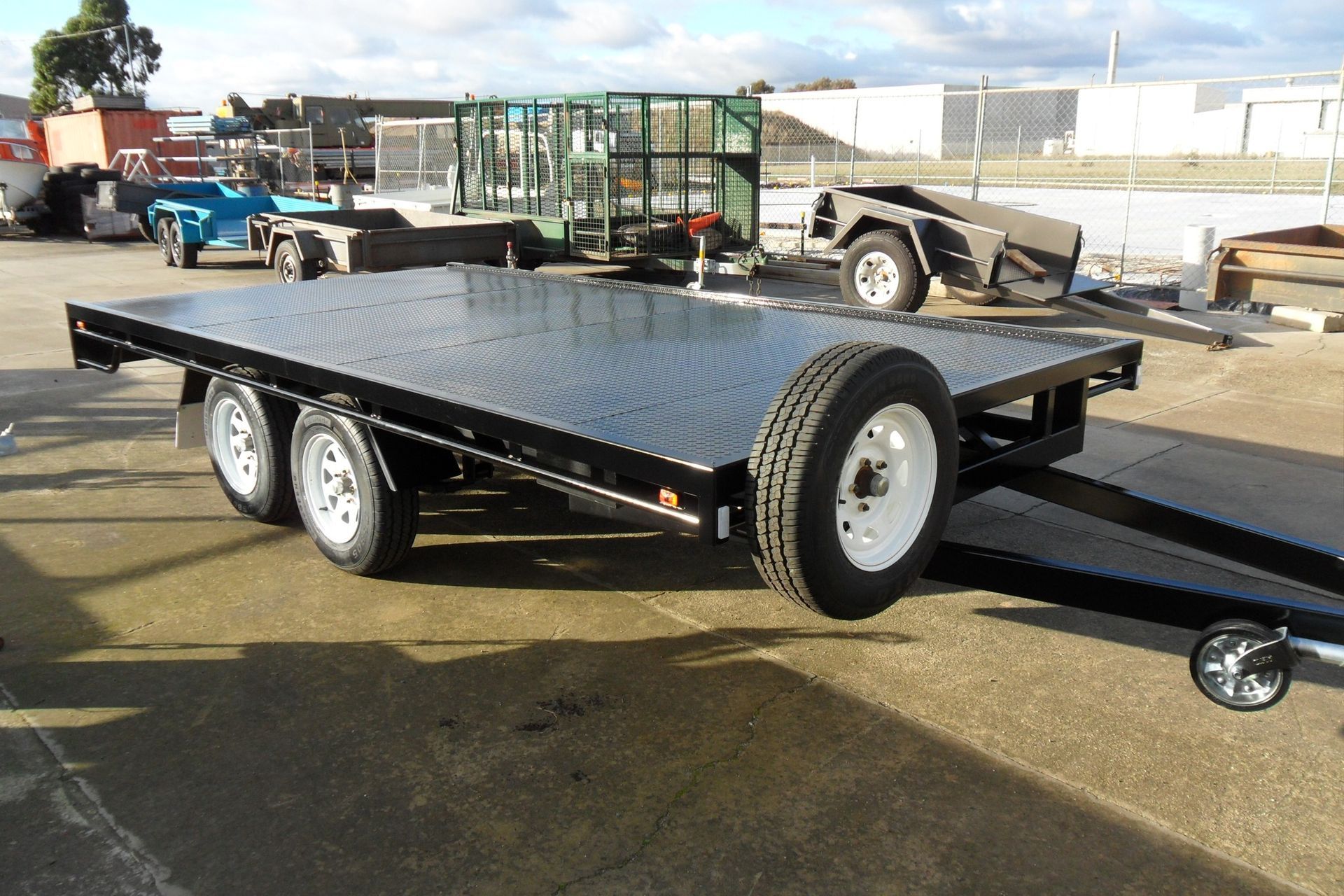 Black flatbed trailer with dual axles and ramp, parked in an industrial lot