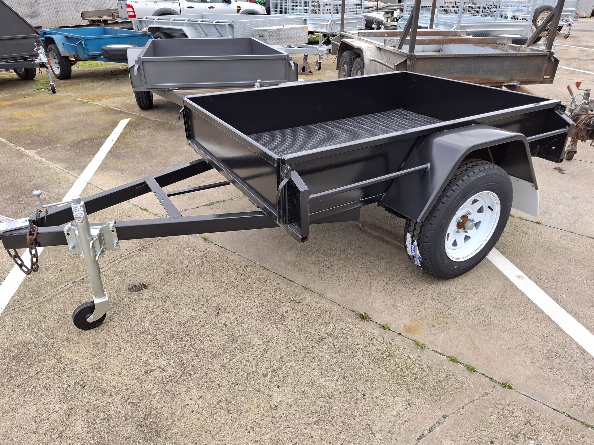 Small black utility trailer with side walls and hitch jack, parked on a wet lot.