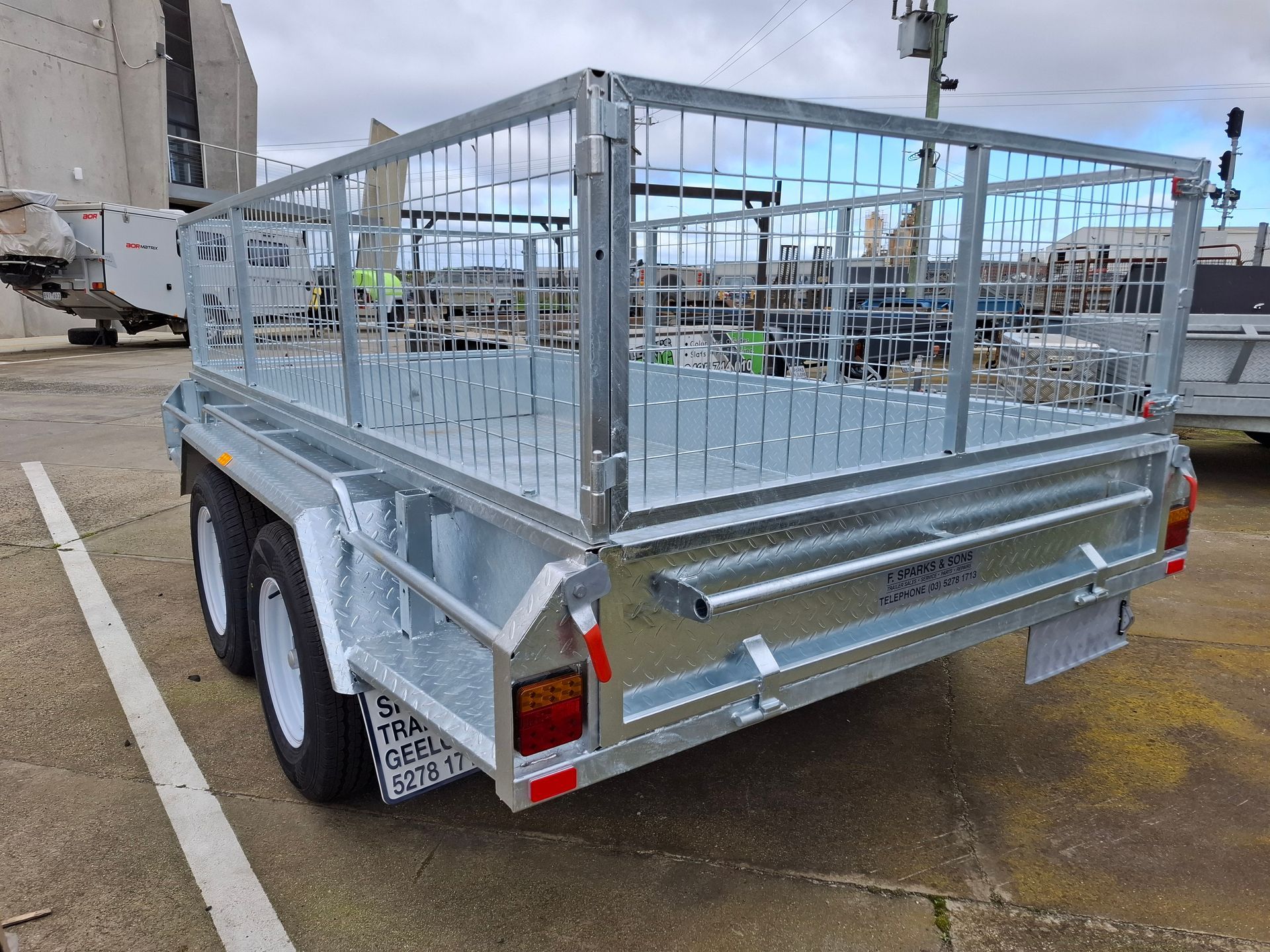 Silver utility trailer with metal cage sides parked on a wet street in an industrial area