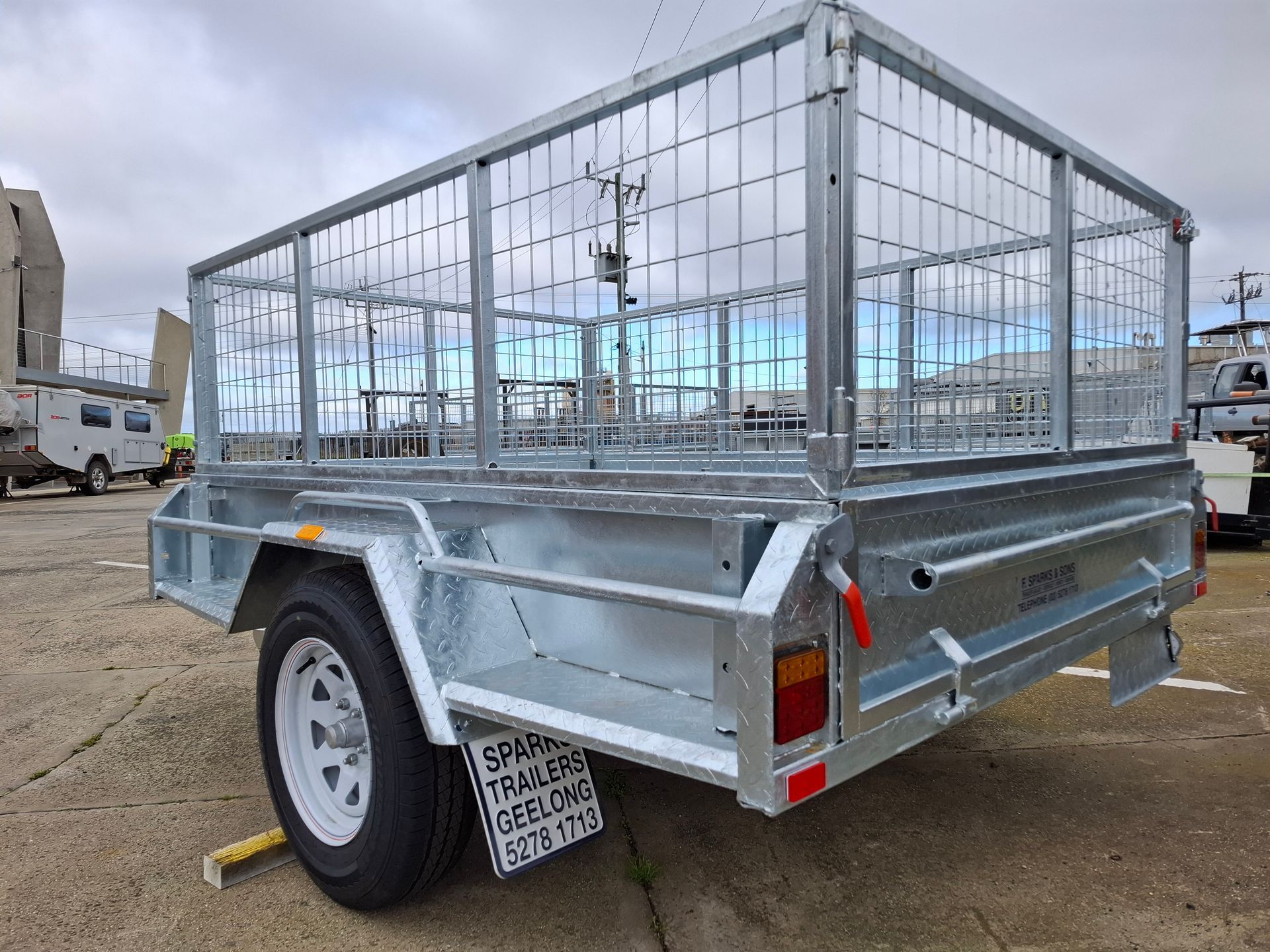 Silver utility trailer with mesh cage sides parked on a gravel lot