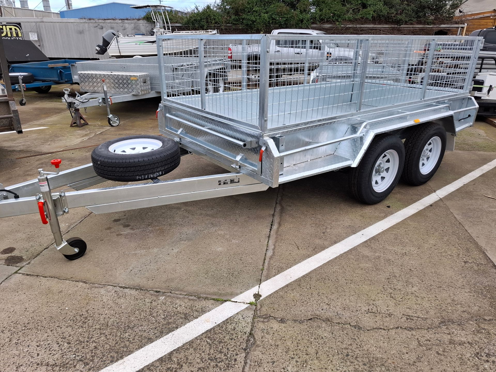 Silver utility trailer with mesh sides and spare tire parked on wet pavement in a lot