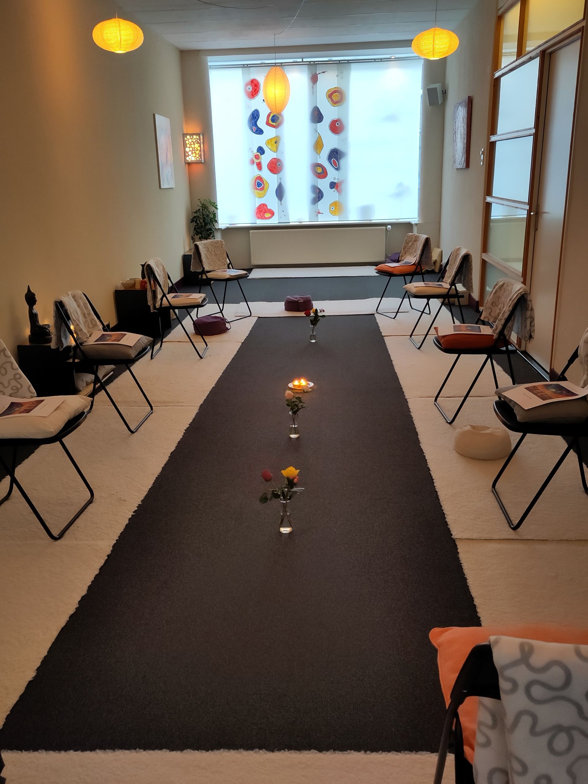 ruimte ingericht met stoelen, bloemen en dekentjes, voor mantra zingen