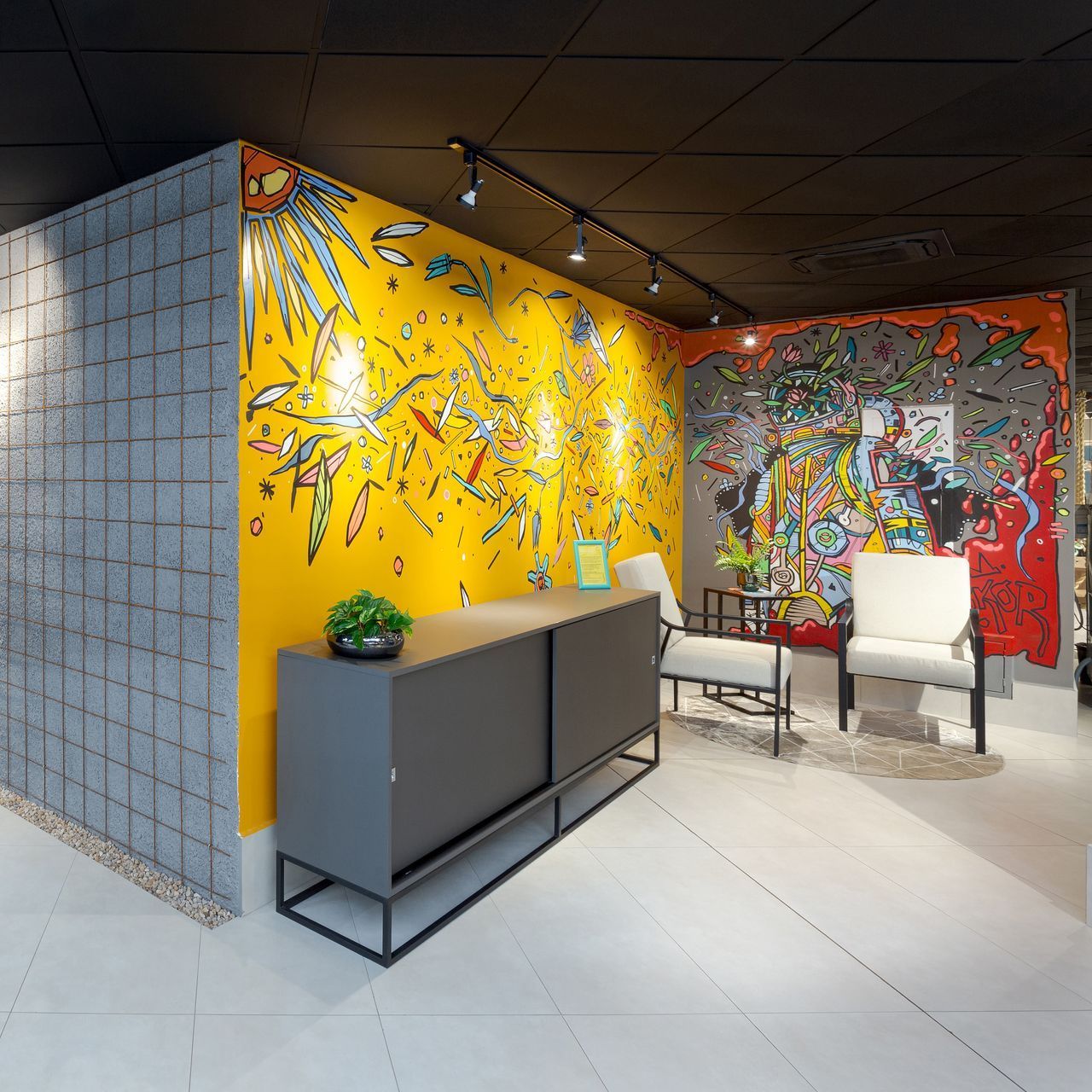 Hall de entrada moderno com murais coloridos nas paredes, balcão de recepção e área de estar.