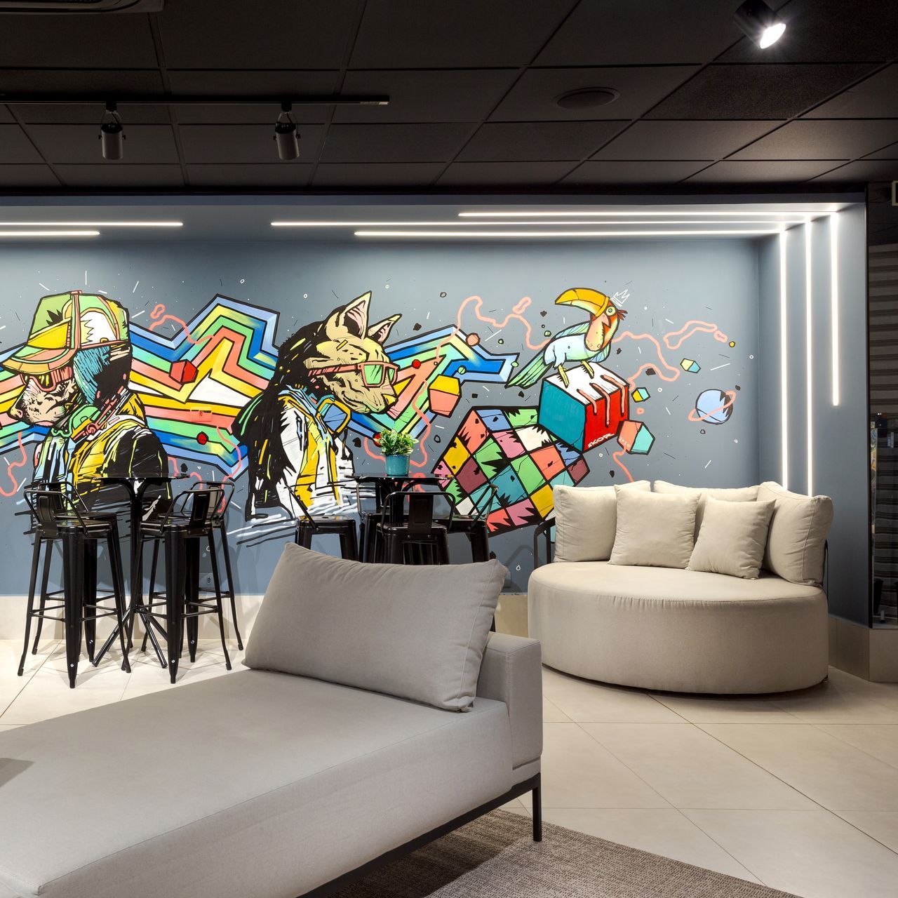 Sala de estar moderna com mural de grafite colorido, banquetas pretas, sofá branco e chaise longue cinza.