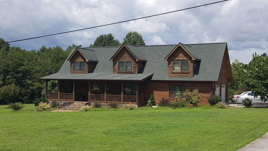 A large log cabin with a green roof is sitting in the middle of a lush green field.