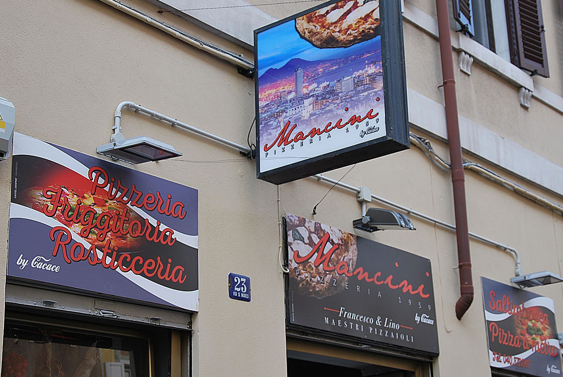 Esterno della Pizzeria e Rosticceria Mancini con insegne del marchio su una parete chiara dell'edificio.