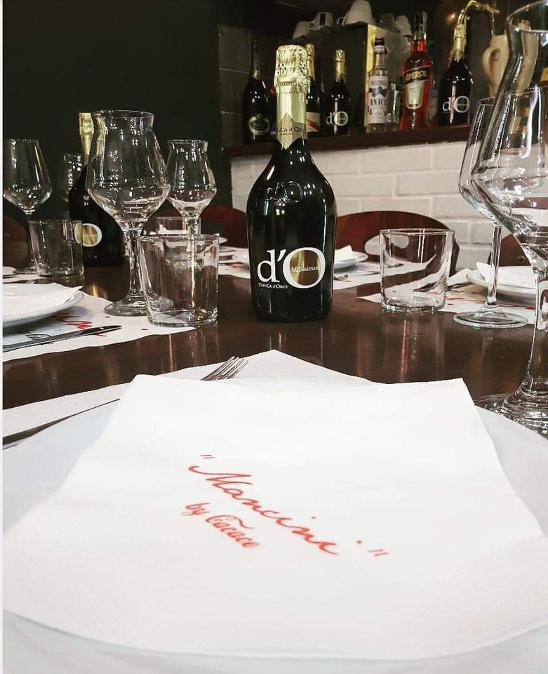 Una tavola apparecchiata in un ristorante con una bottiglia di vino d'O, bicchieri e un piatto con un tovagliolo di marca.