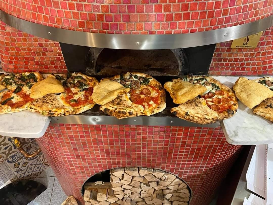 Diverse pizze cuociono all'interno di un forno a legna rivestito di piastrelle a mosaico rosse.