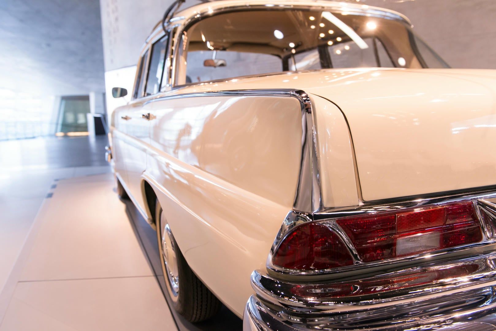 Cream-colored vintage car on display in a modern museum.