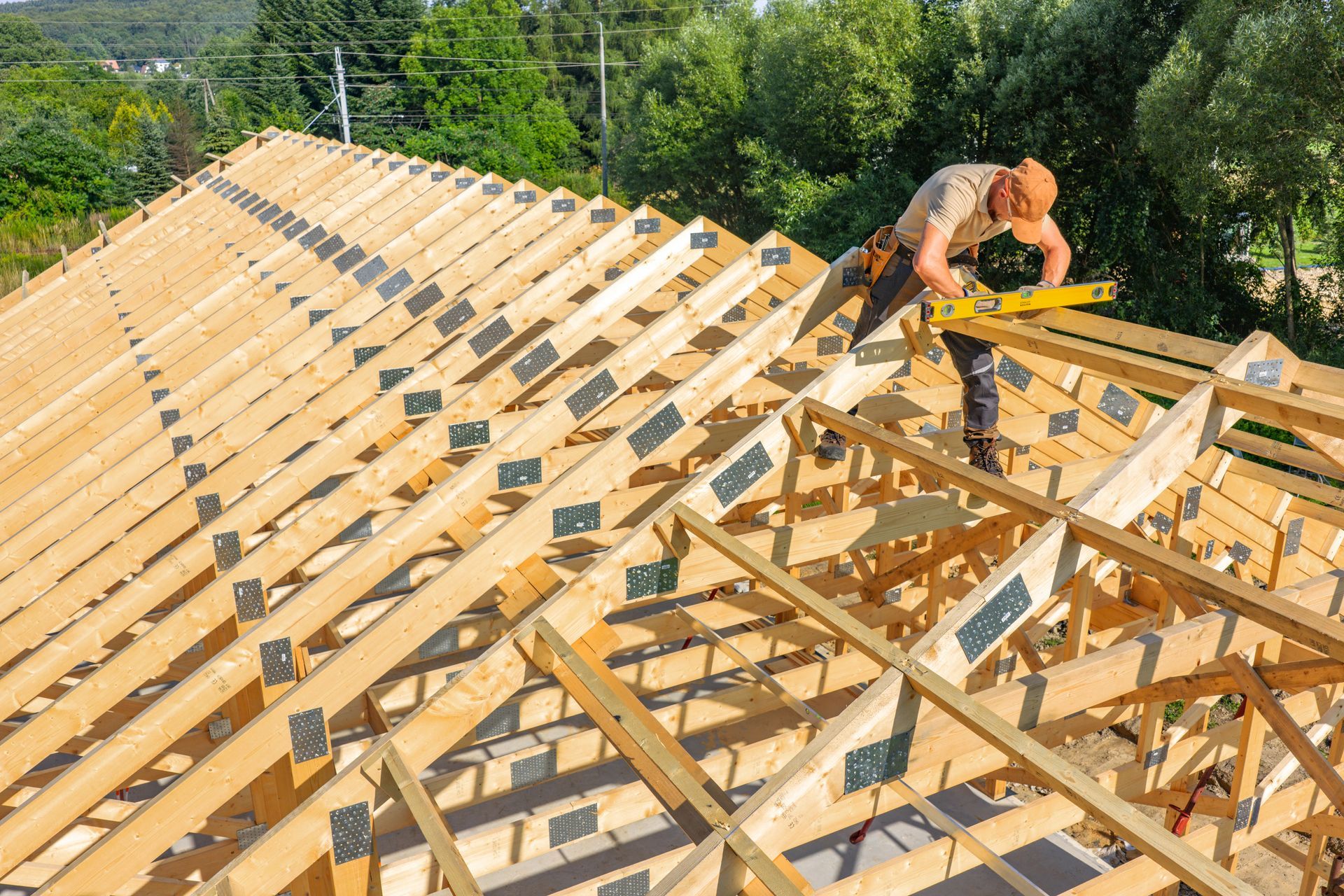 A construction worker carpenter measuring roof trusses on a sunny day outdoors.
