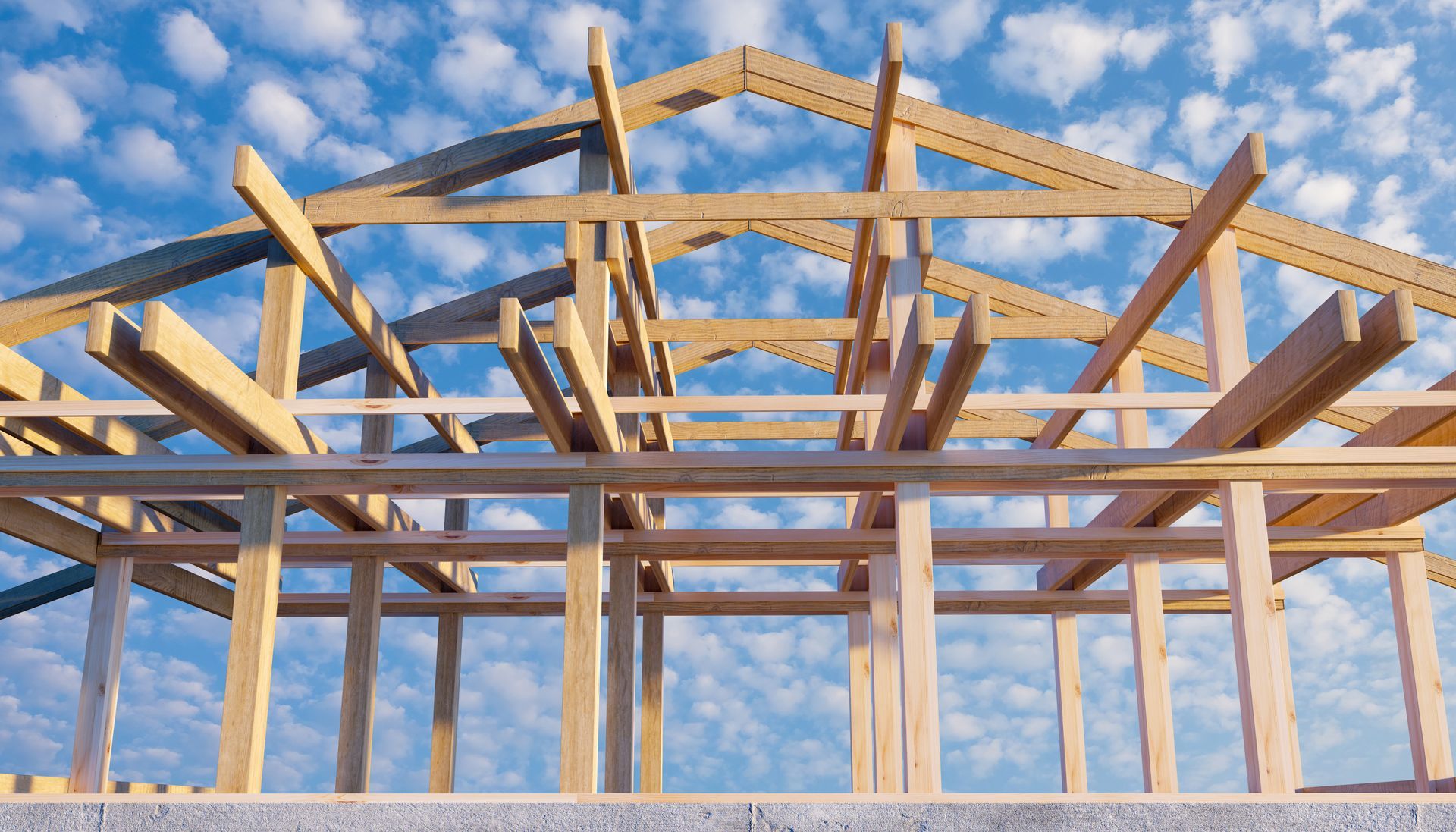 Wooden house frame against a bright sky, showing structural beams and roof trusses.