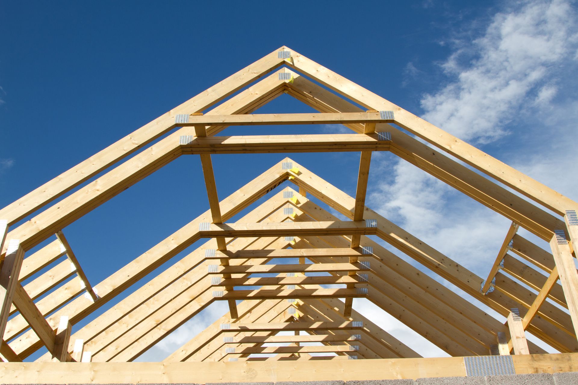 View from the bottom up of wooden roof trusses against a blue sky.