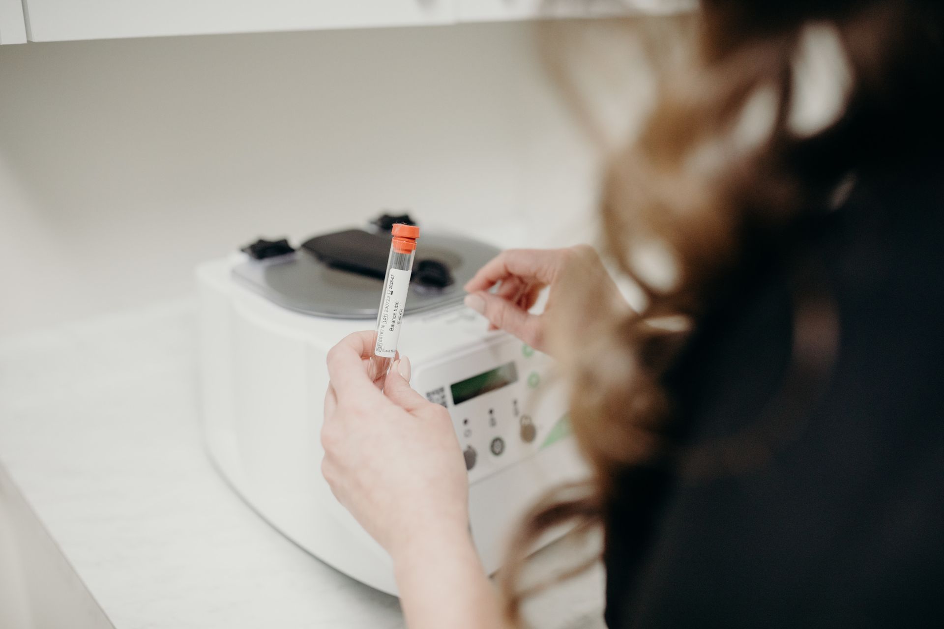 A woman is holding a test tube in front of a machine.