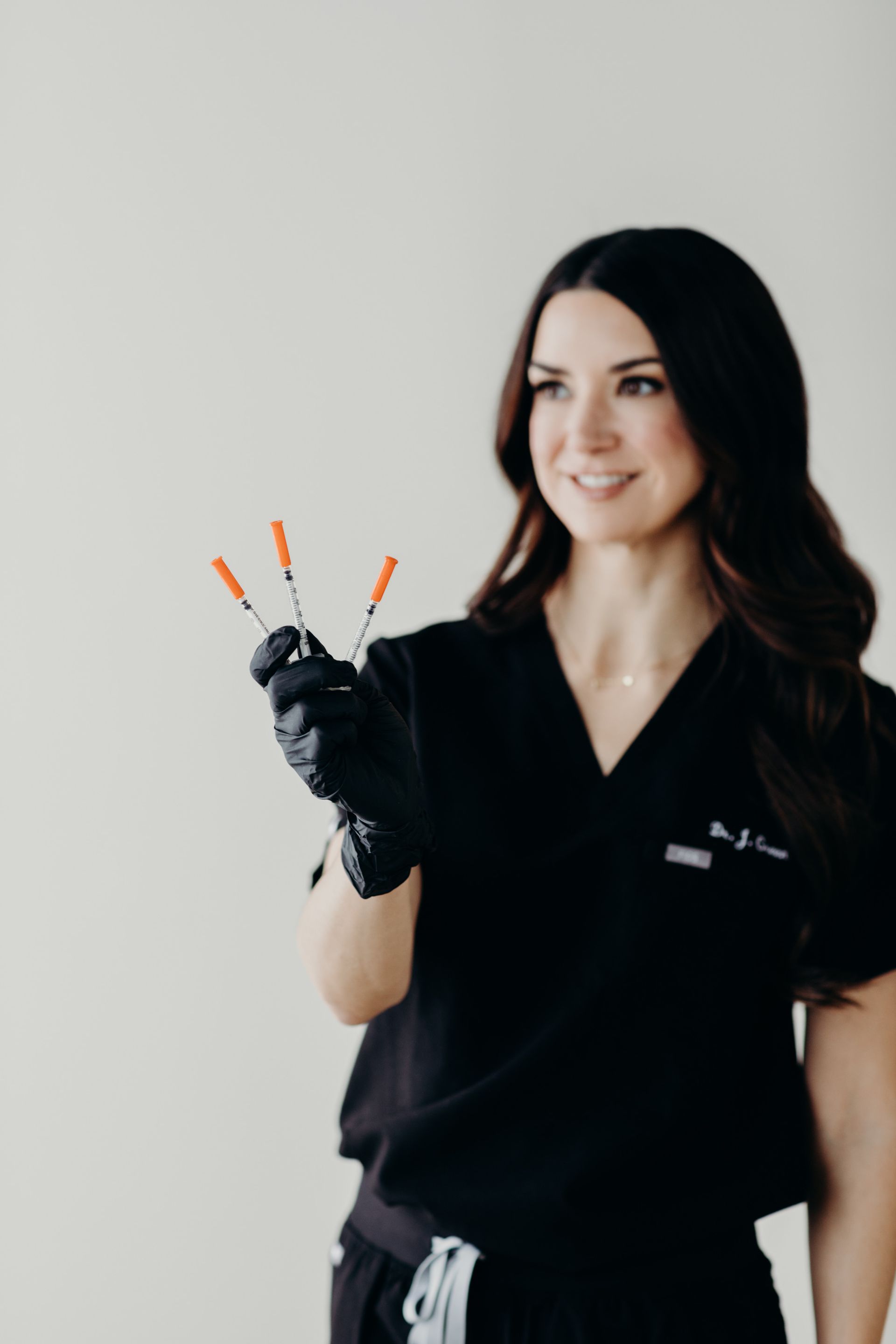 A woman in a black scrub top is holding three syringes in her hand.