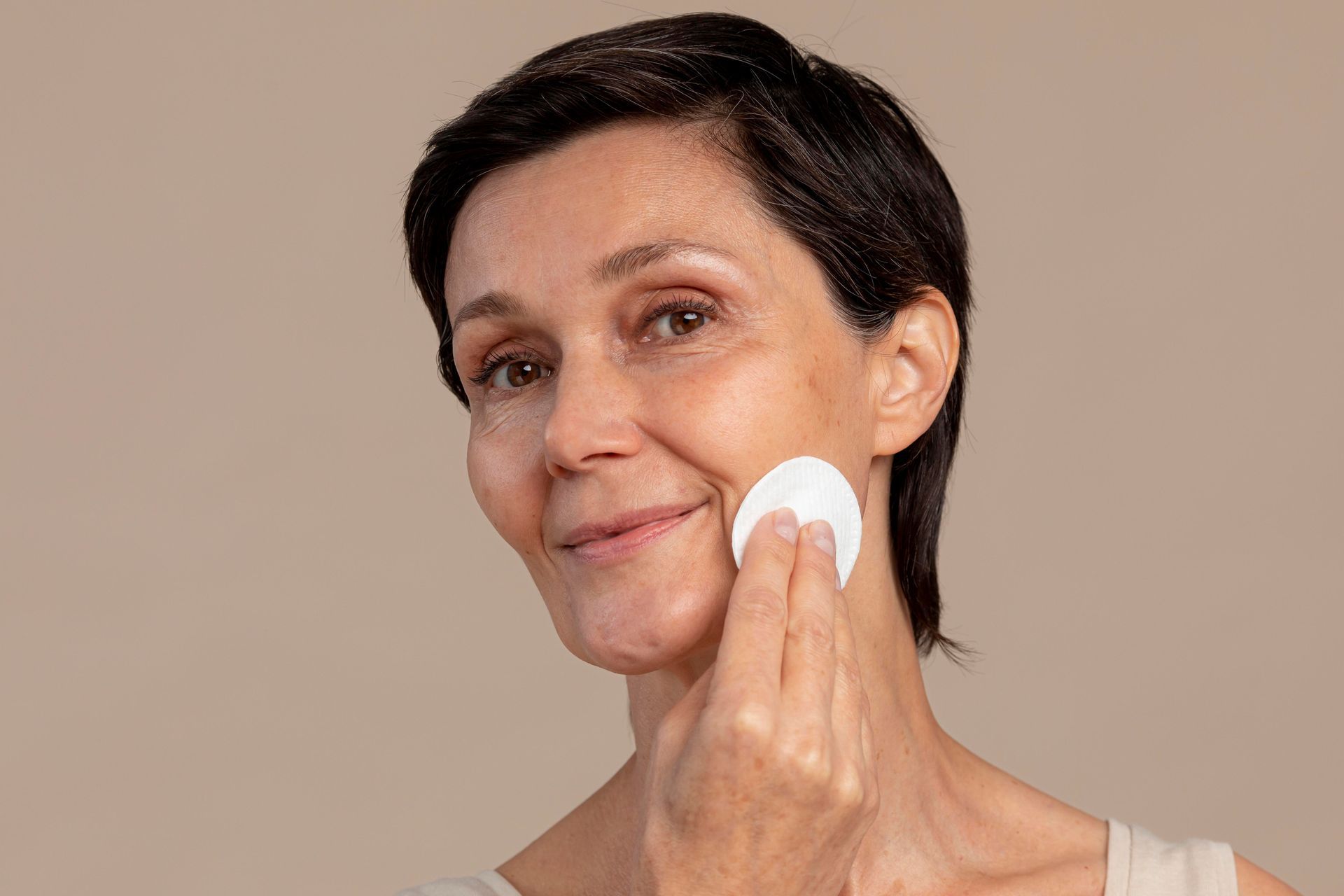 A woman is cleaning her face with a cotton pad.